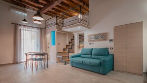 Ein geräumiger Wohnbereich mit hoher Decke, einem Esstisch mit Stühlen, einem türkisfarbenen Sofa und einer Treppe, die zu einer oberen Ebene führt.