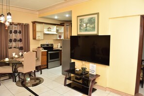 A dining area with a table and chairs, a kitchen with appliances, and a flat-screen TV mounted on the wall. - Embassy royal. Kick back and relax at this modern Spacious family friendly  home (Kingston)