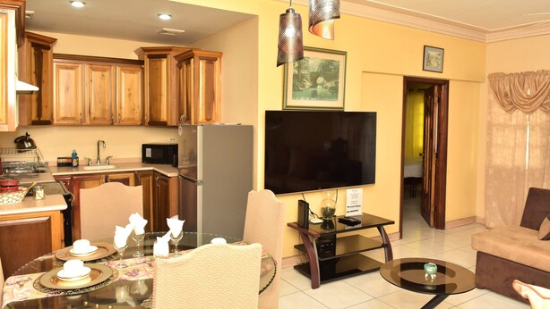 Una cocina moderna con armarios de madera, un comedor con mesa de vidrio y una sala de estar con sofá y televisor.