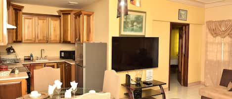 Una cocina moderna con armarios de madera, un comedor con mesa de vidrio y una sala de estar con sofá y televisor.