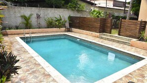 Una piscina rectangular con borde alicatado, rodeada por un solárium con losetas de piedra.