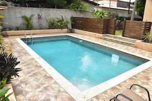 A rectangular swimming pool with a tiled edge, surrounded by a stone-tiled deck. - Embassy royal. Kick back and relax at this modern Spacious family friendly  home (Kingston)