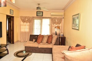 A living room with a sofa, a coffee table, a TV, and a ceiling fan. - Embassy royal. Kick back and relax at this modern Spacious family friendly  home (Kingston)