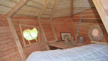 Ein Schlafzimmer im Holz-Giebelgeschoss mit Bett, kleinem Tisch, Fenster mit Blick auf Grünflächen und einer Zierlaterne.