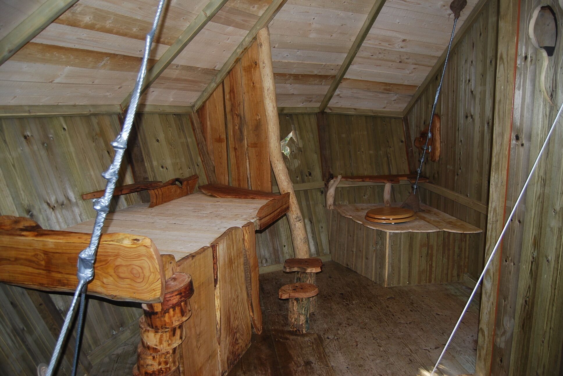 A rustic wooden room with a sloped ceiling, wooden benches, and a simple wooden stool.