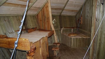 A rustic wooden room with a sloped ceiling, wooden benches, and a simple wooden stool.