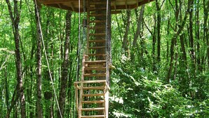 A wooden treehouse with a ladder, surrounded by a dense forest. - Le Parc de la Belle (Magné)