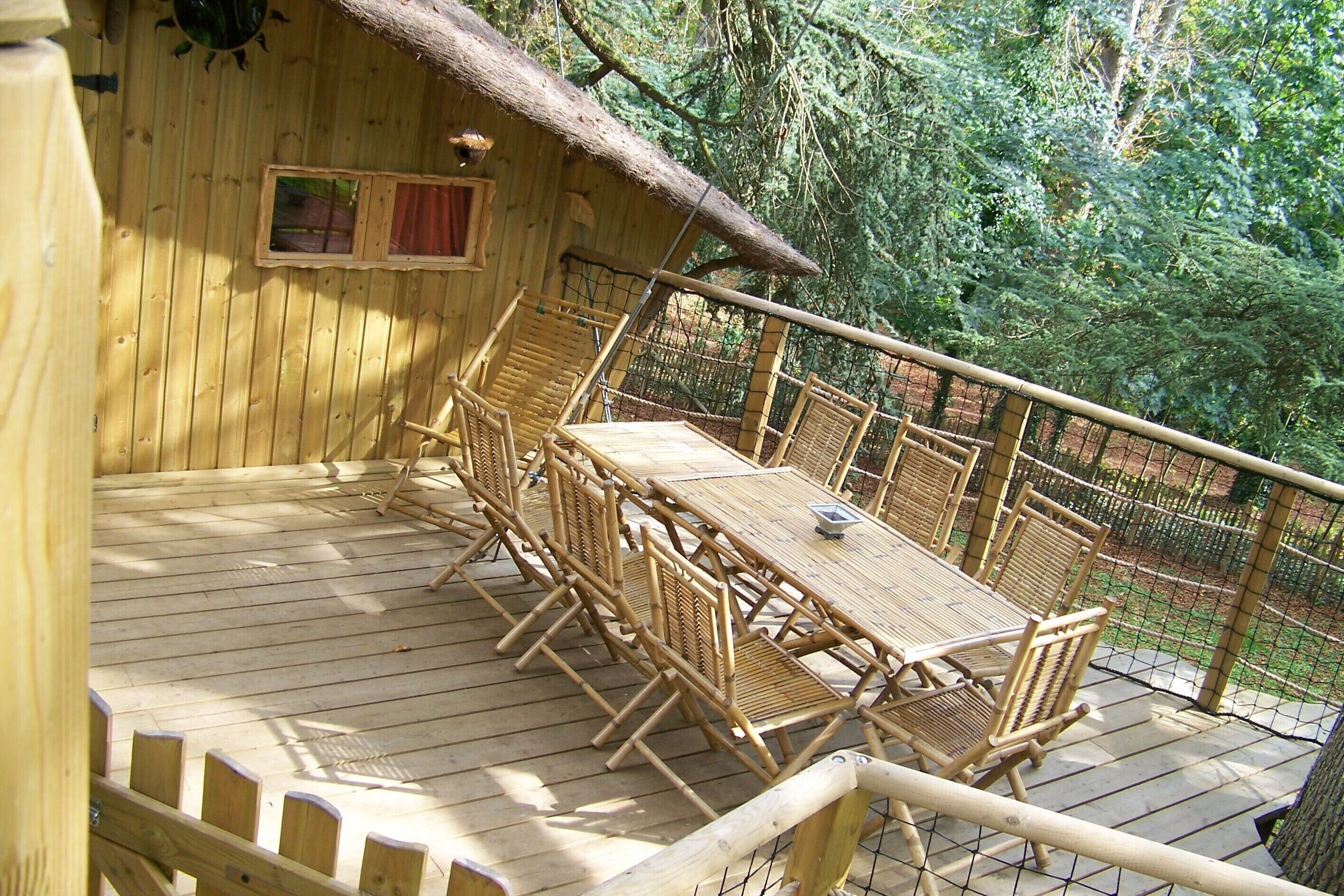 A wooden deck with a table and chairs, surrounded by a wooden fence and trees.