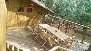 A wooden deck with a table and chairs, surrounded by a wooden fence and trees.
