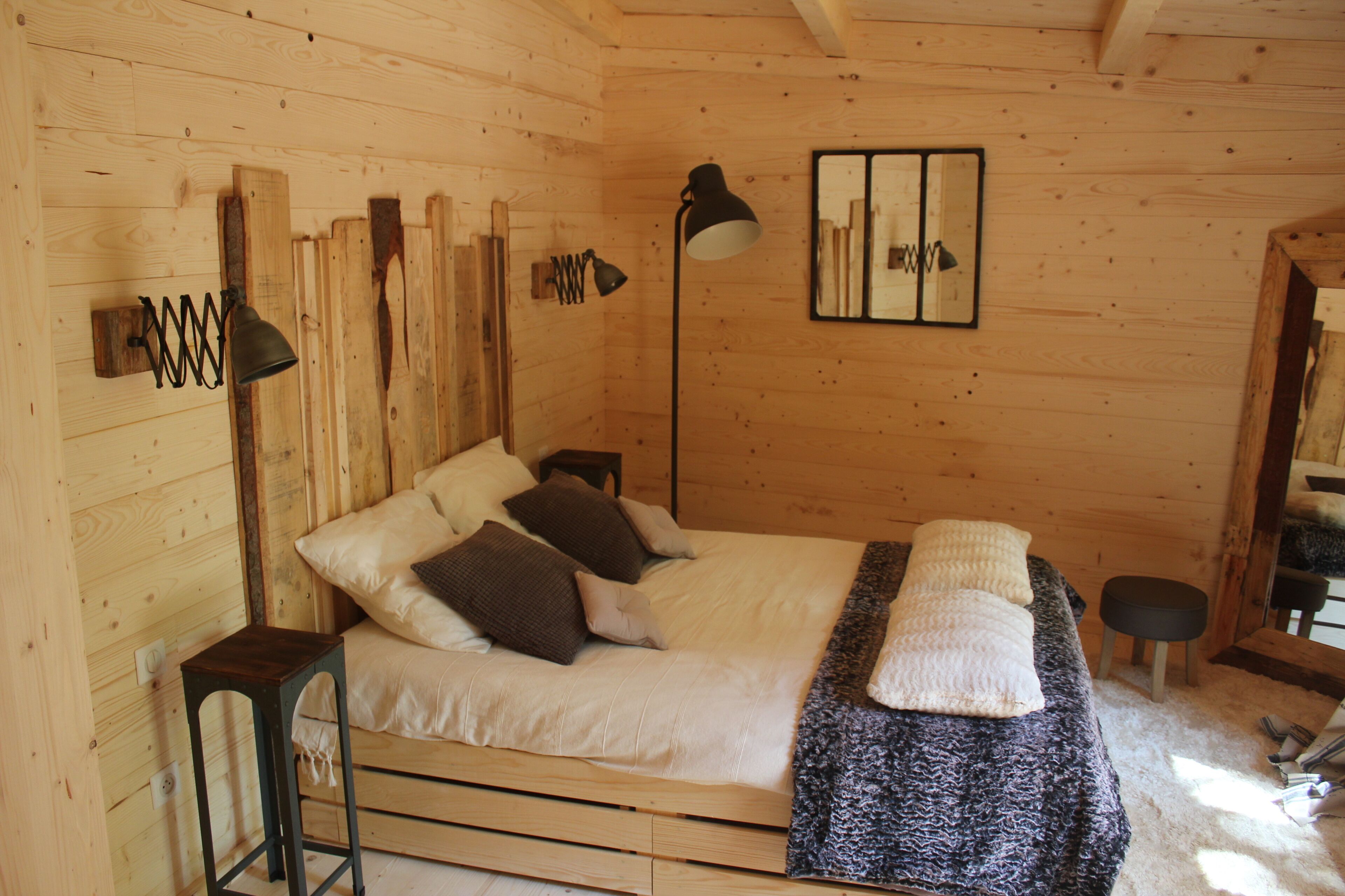 A wooden room with a bed, two lamps, and a mirror on the wall.
