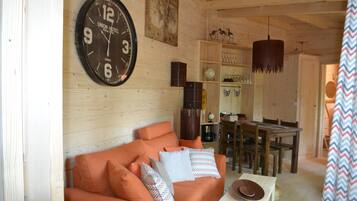 A wooden interior with a sofa, a dining table, and a clock on the wall.
