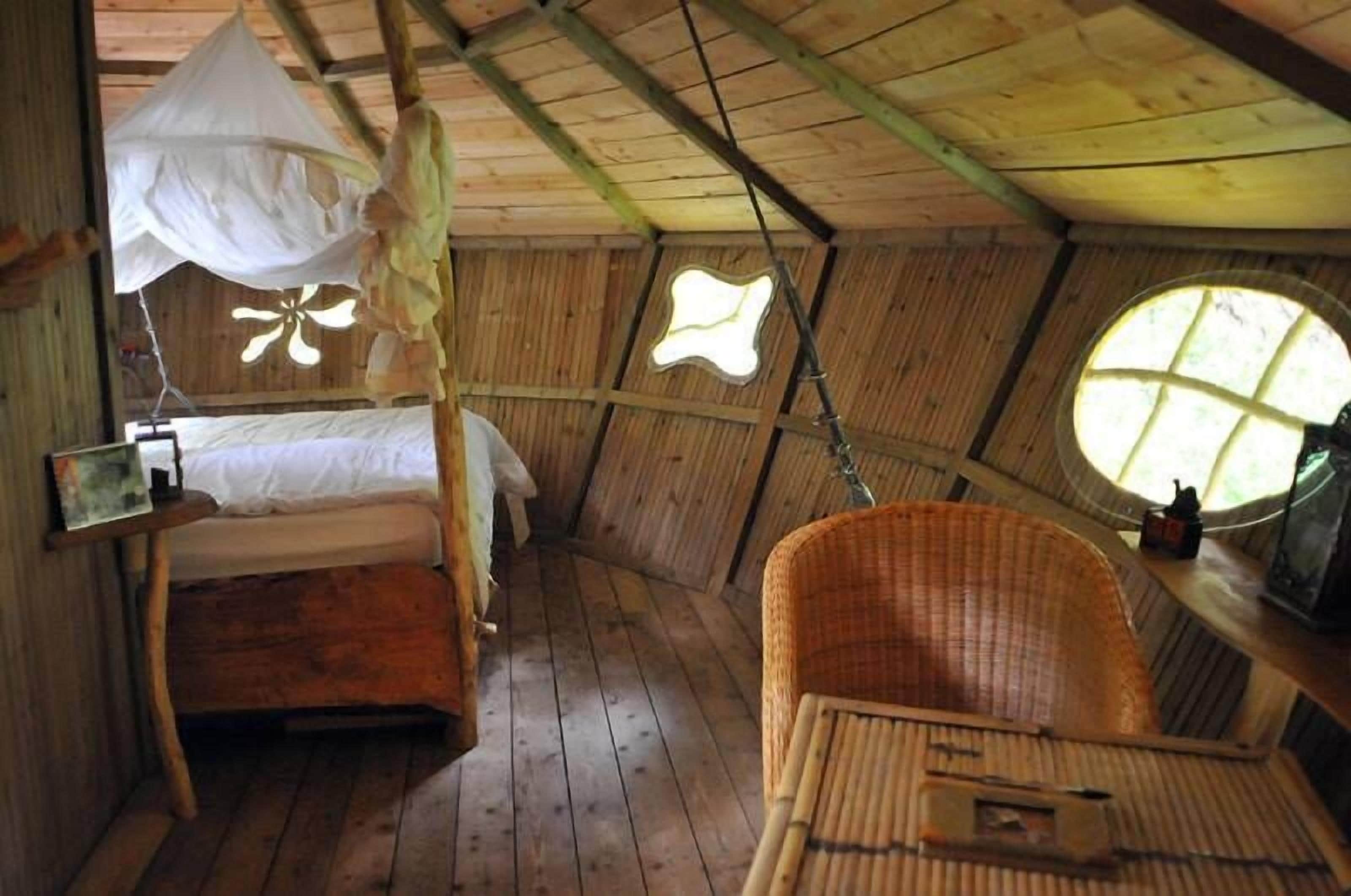 A wooden room with a bed, a wicker chair, and a window.