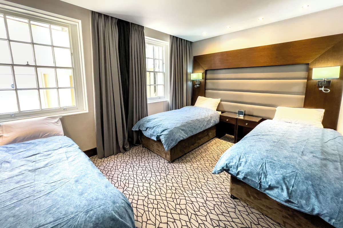 A hotel room with two beds, a large window with curtains, a headboard with built-in lighting, and a patterned carpet.