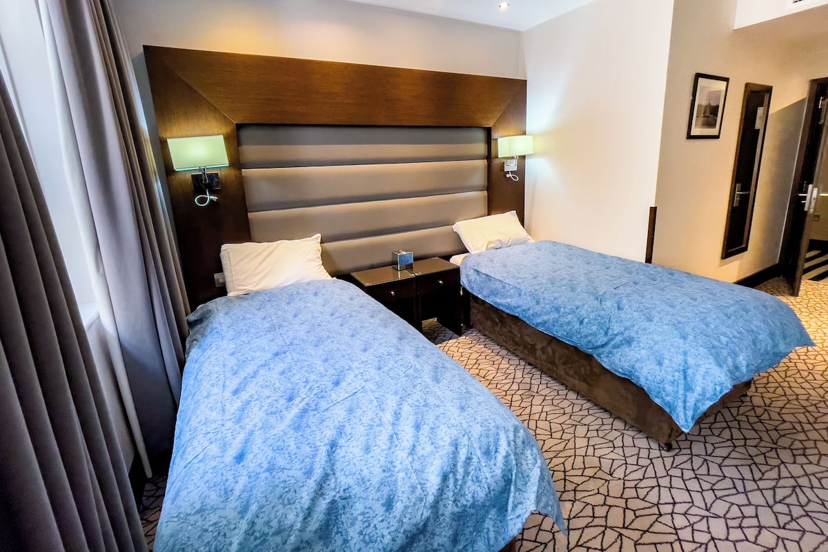 A hotel room with two beds, a wooden headboard, bedside lamps, and a patterned floor.