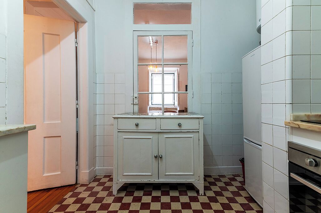 Eine Küche mit Schachbrettboden, einem weißen Schrank mit zwei Türen, einem Fenster mit Blick und einem Kühlschrank.