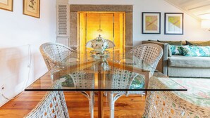 Ein Essbereich mit Glastisch und Korbstühlen, eine Couch mit gemusterten Kissen und gerahmte Kunstwerke an den Wänden.