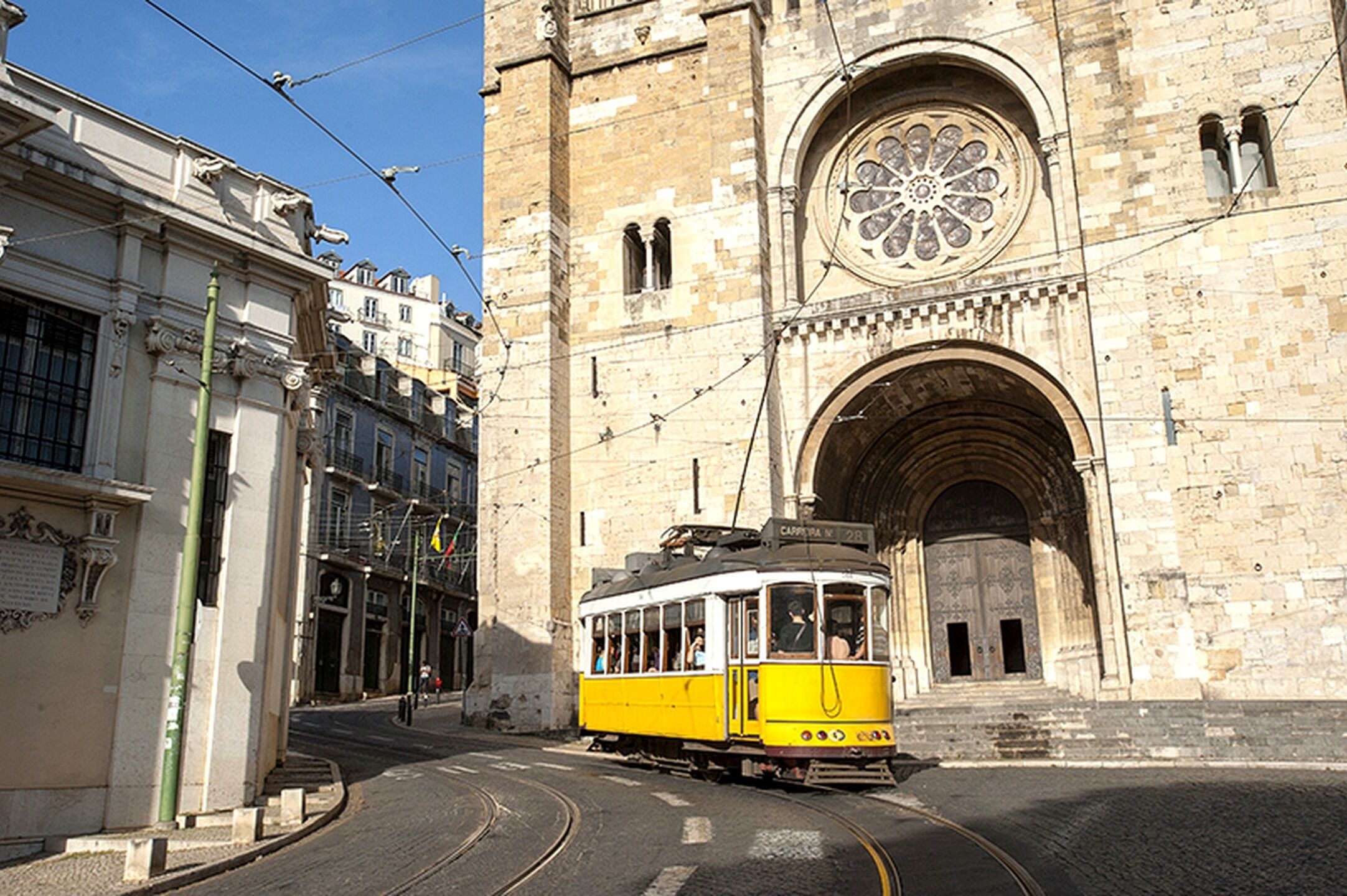 Un tram giallo in una stazione, con un grande edificio decorativo sullo sfondo.