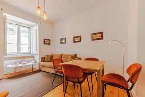 A dining area with a wooden table, orange chairs, a sofa, and a window with natural light.