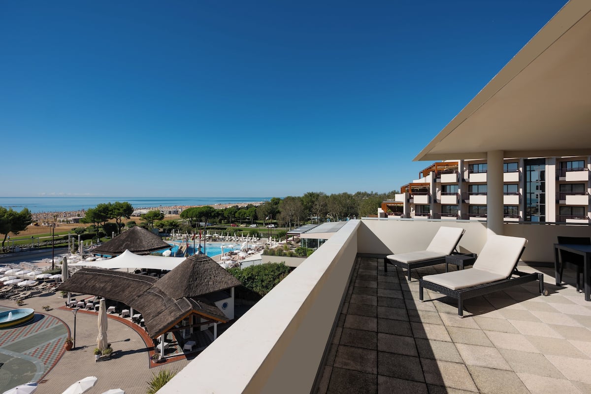 A rooftop terrace with lounge chairs overlooking a pool and beach.