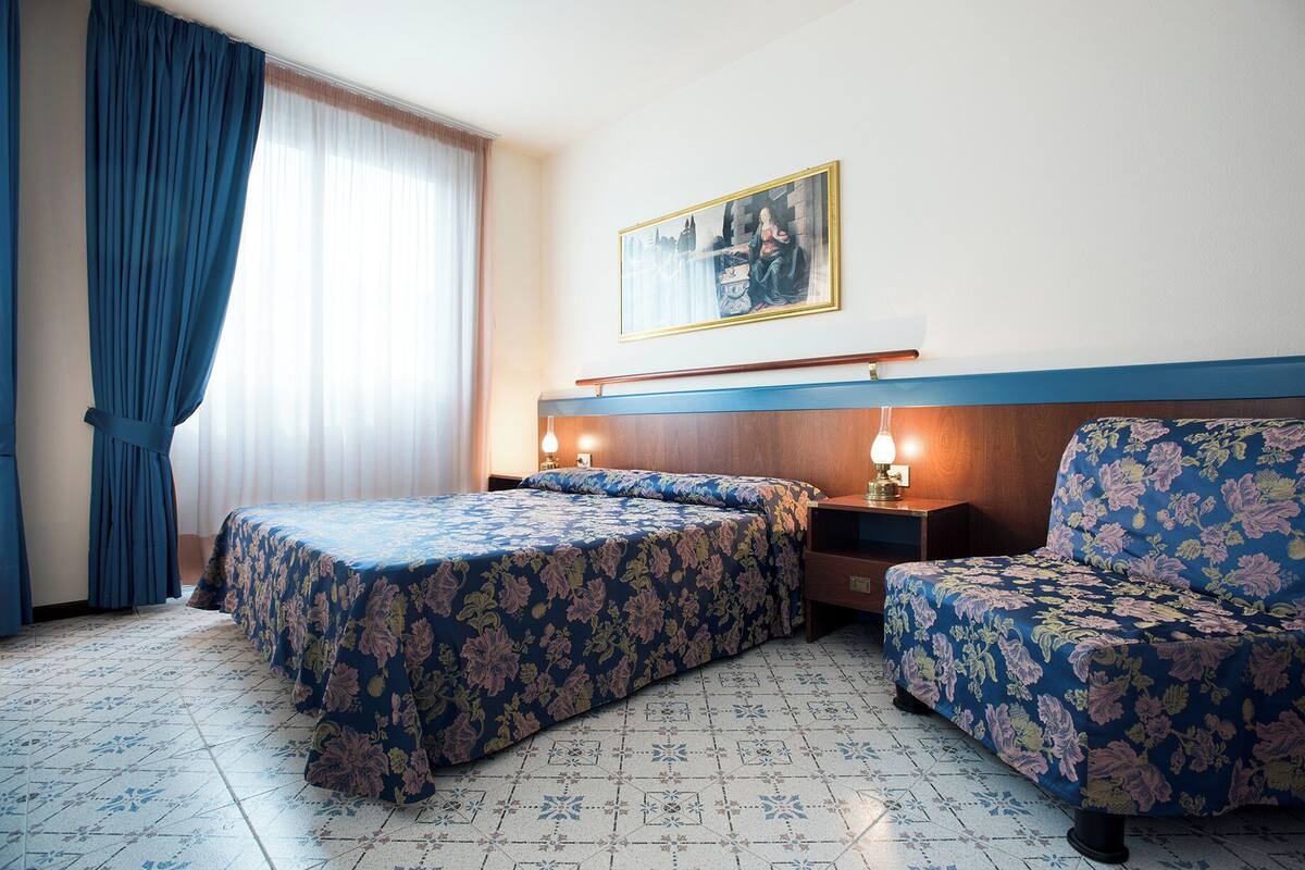 A hotel room with two beds, a sofa, a painting on the wall, and a window with curtains.