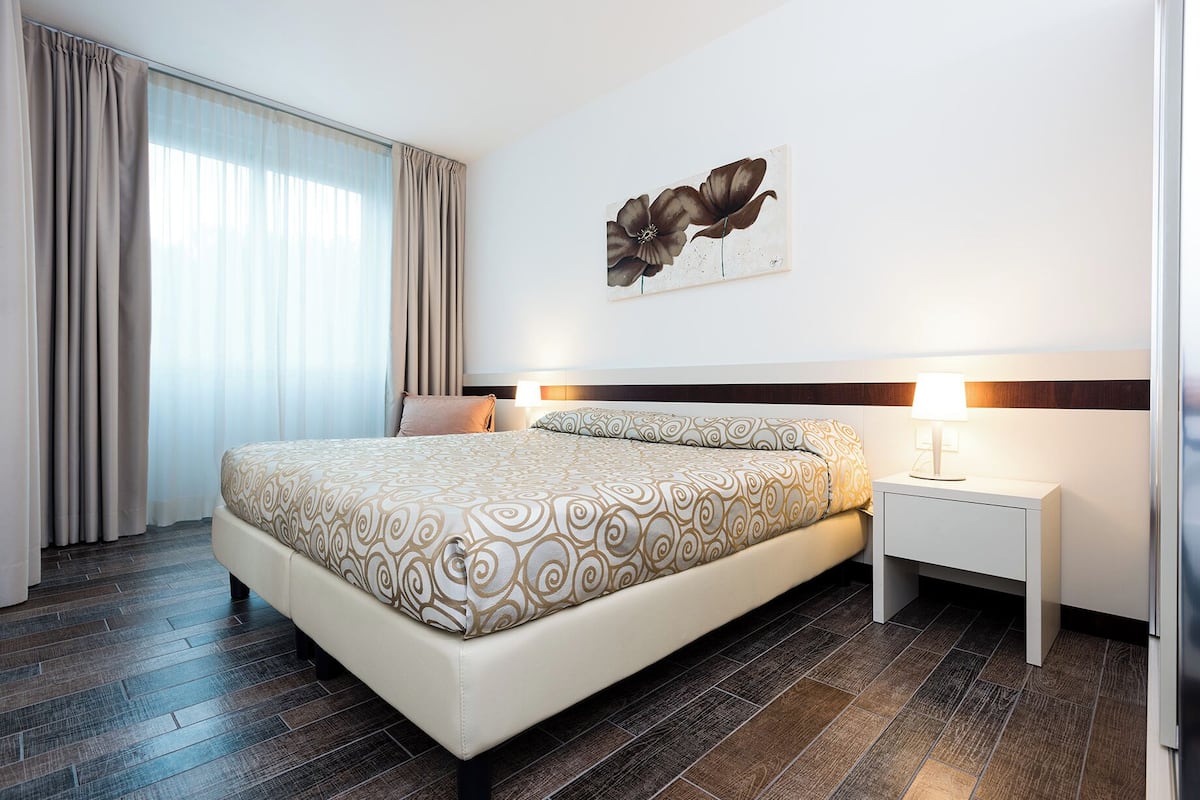 A modern hotel room with a large bed, a nightstand, and a wall-mounted artwork.