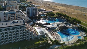 Une vue aérienne d’un complexe hôtelier doté de plusieurs piscines, d’une plage et, au loin, d’un paysage urbain.