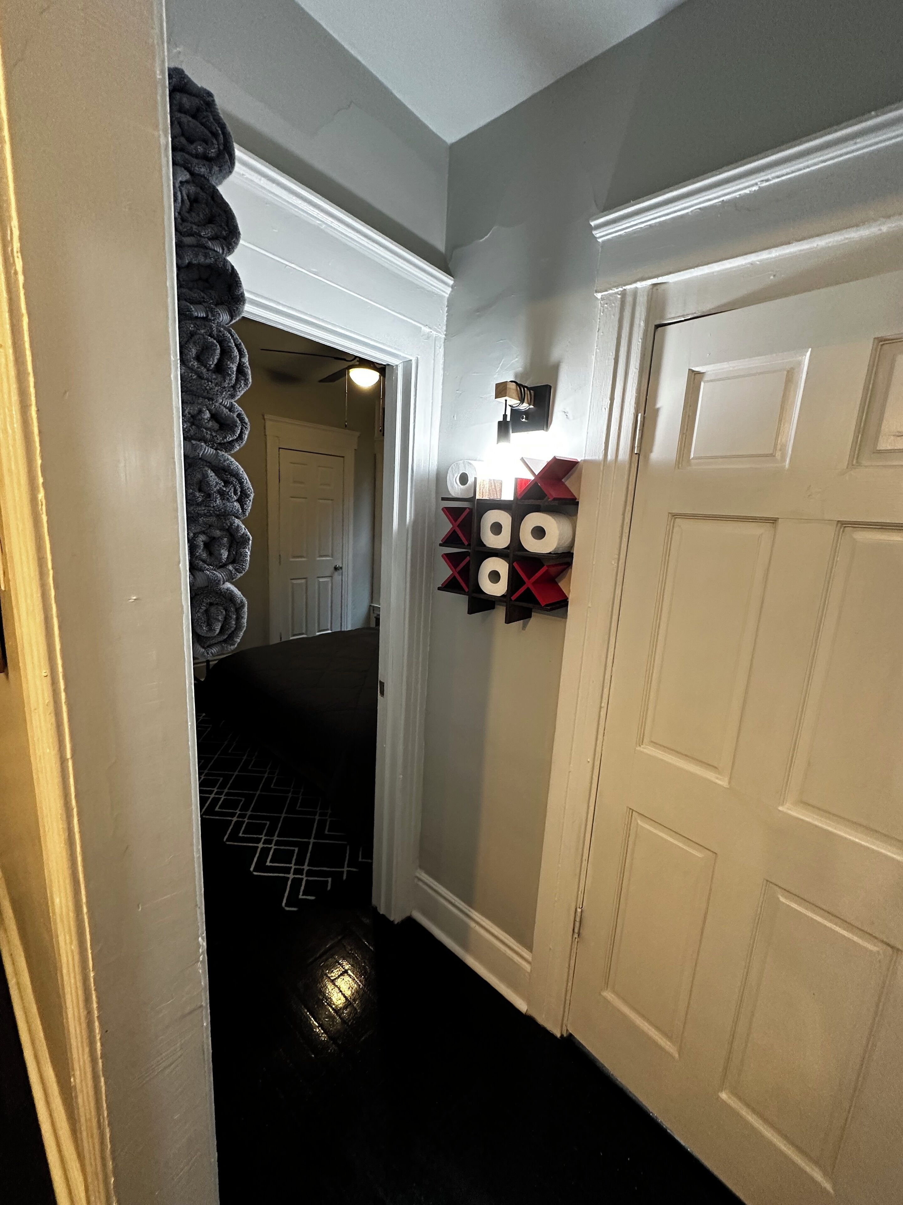 A hallway with a white door, a wall-mounted shelf with toilet paper, and a patterned rug on the floor.