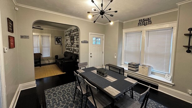 A dining area with a black table and chairs, a chandelier, and a brick wall.