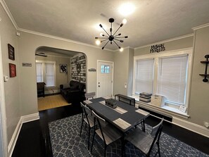 Un coin repas avec une table et des chaises noires, un lustre et un mur en briques.