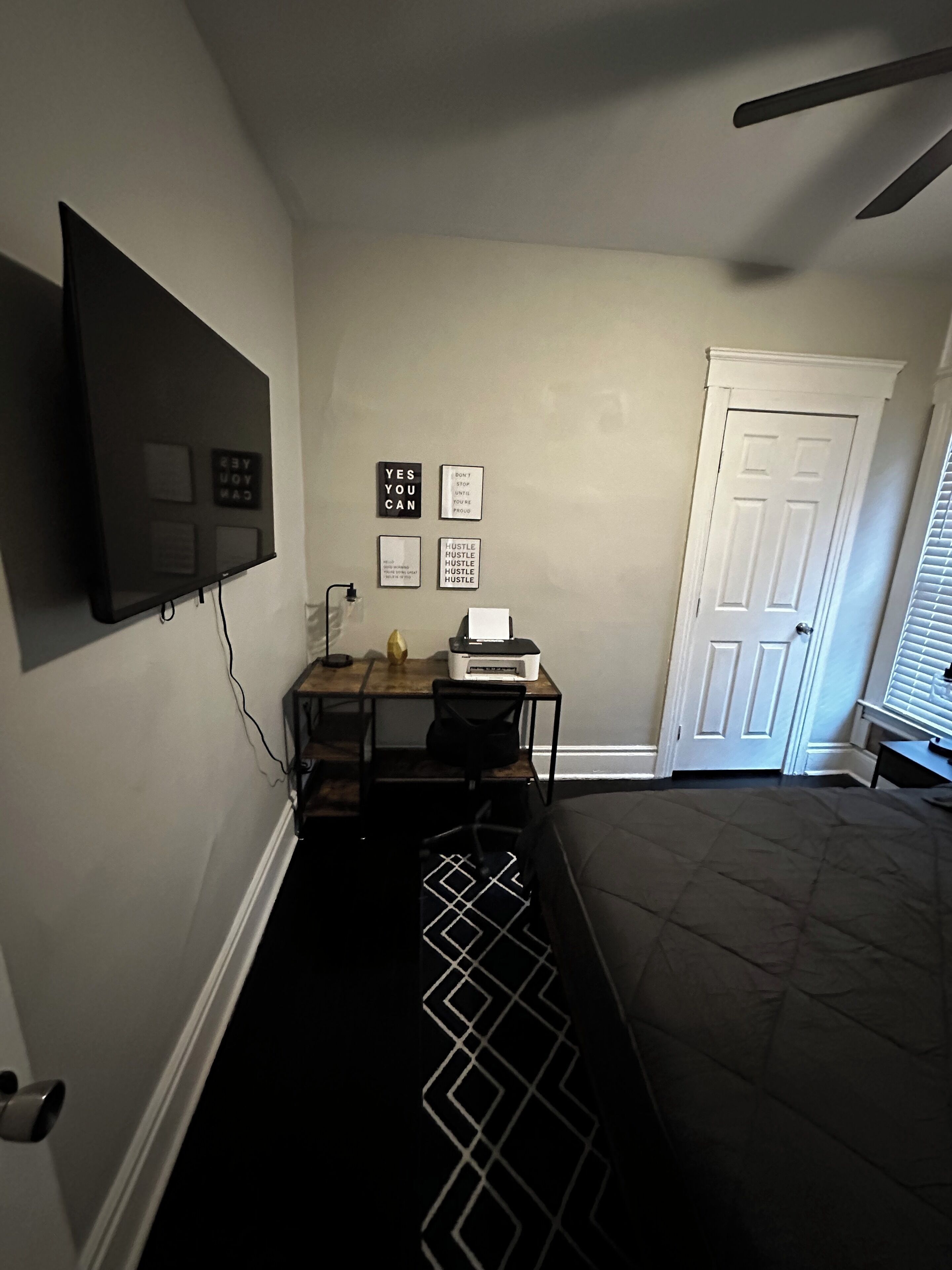 Een kamer met een bed, een bureau met een printer, een aan de muur bevestigde televisie en motiverende posters.