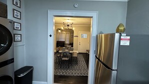 A kitchen with a stainless steel refrigerator, a trash can, and a dining area with a patterned rug.