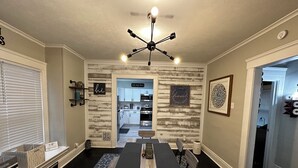 A dining area with a dark wood table and chairs, a modern chandelier, and a view into the kitchen.