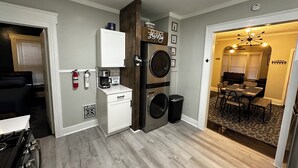 A compact kitchen with a coffee maker, a microwave, and a sink. There is a dining area with a table and chairs visible through an open doorway.