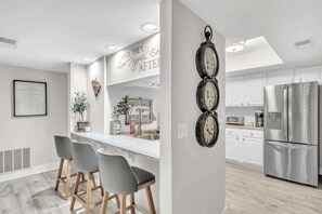 Cozinha moderna com área de bar, eletrodomésticos de aço inoxidável e um relógio na parede.