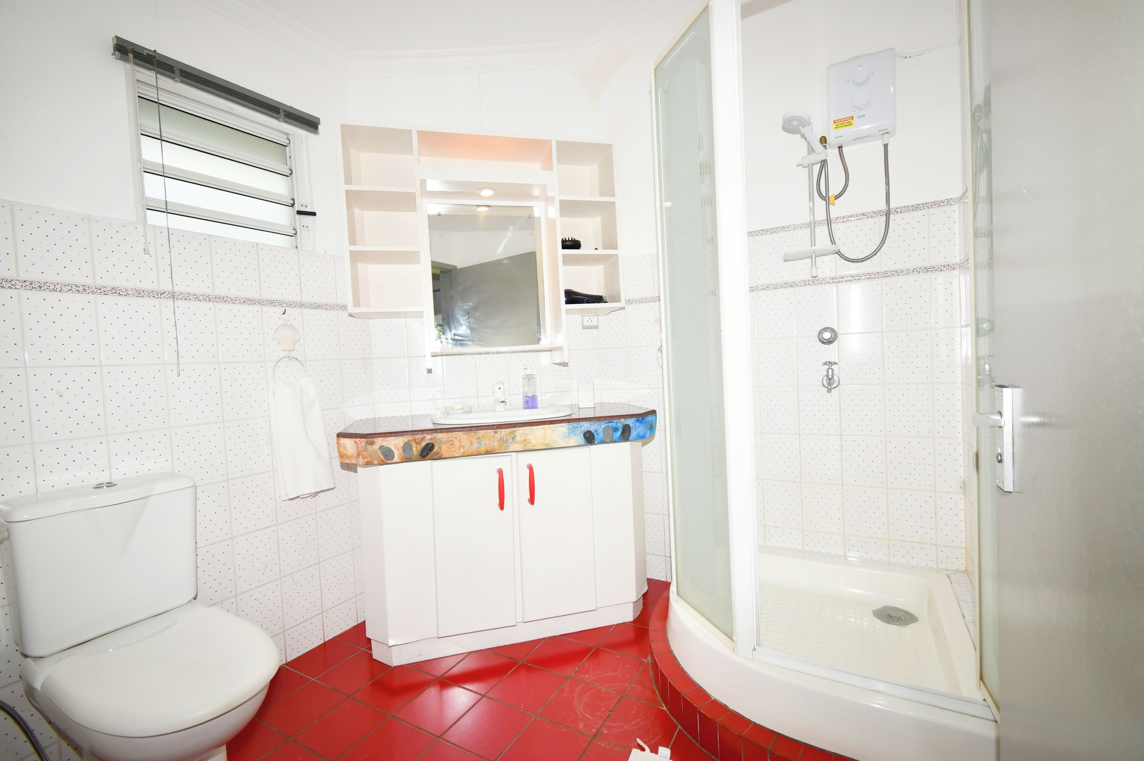 A bathroom with a toilet, a sink with a mirror, and a shower area.