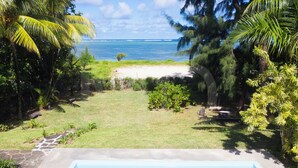 A swimming pool with a view of the ocean and a grassy area with palm trees.