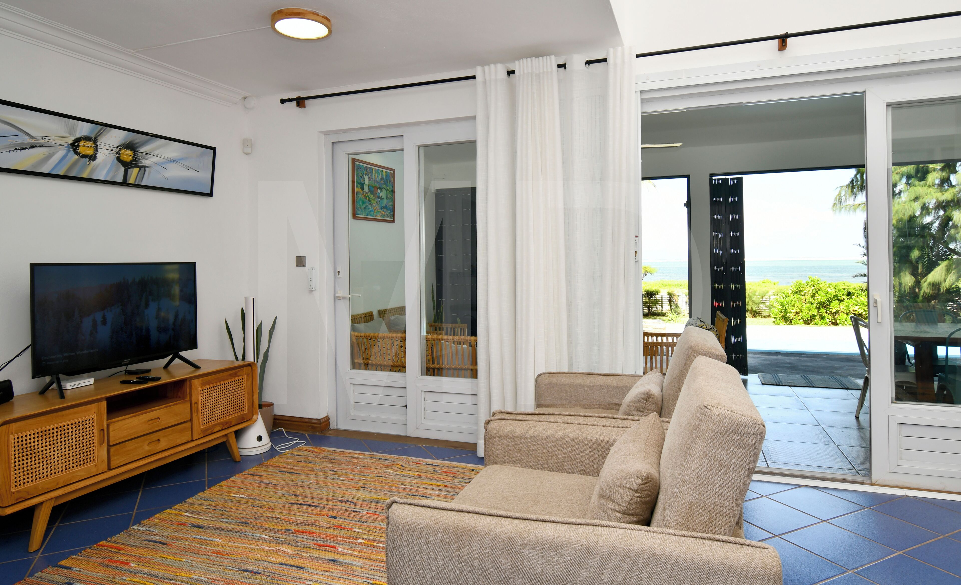 A living room with a television, sofa, and a view of the ocean through a sliding glass door.