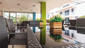 A modern outdoor seating area with wicker furniture, a green pillar, and a view of a white building with balconies. - EL PARAISO HOTEL CAMPESTRE (La Virginia)