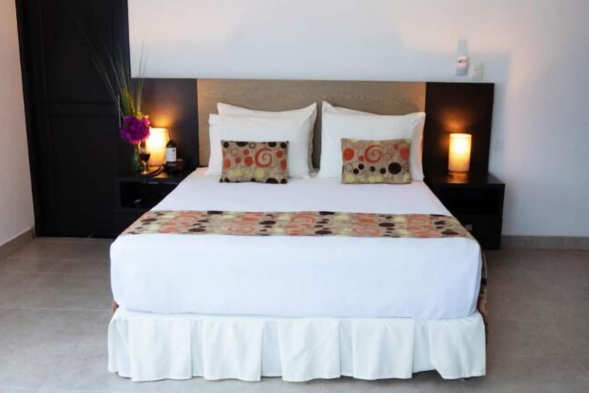 A neatly made bed with white bedding and decorative pillows, flanked by two bedside tables with lamps and a vase of flowers.