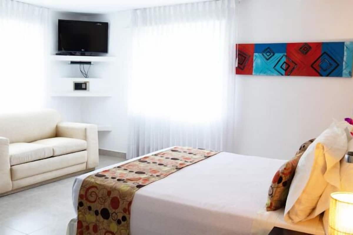 A hotel room with a bed, a sofa, a TV mounted on the wall, and a painting on the wall.