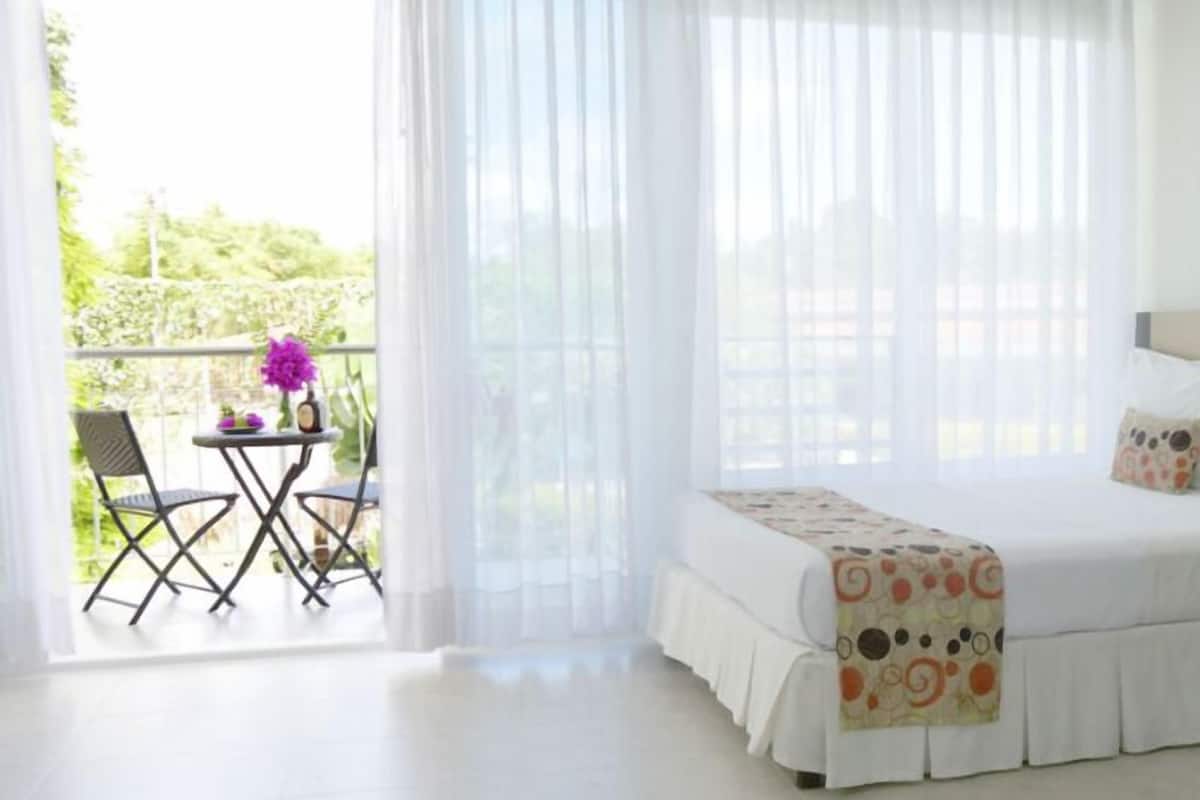 A bedroom with a bed, a small table with a chair, and a view of greenery outside.