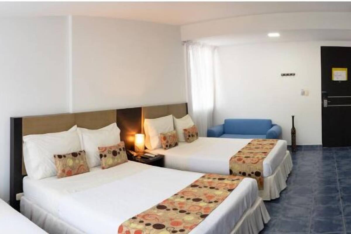 A hotel room with two beds, a blue sofa, and a nightstand with a lamp.