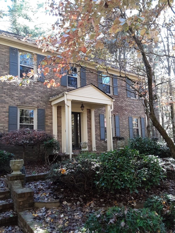 A two-story brick house with a front porch, a stone staircase, and a garden with leaf-covered ground. - Beautiful 2-story home minutes from Downtown Hendersonville (Laurel Park)