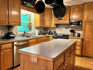 A kitchen with wooden cabinets, a stainless steel dishwasher, a double sink, a microwave, a stove, and a toaster.
