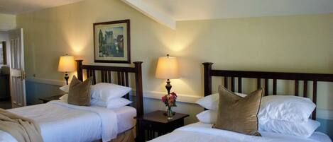 A hotel room with two beds, each with white linens and brown pillows. There are two bedside lamps and a framed picture on the wall.