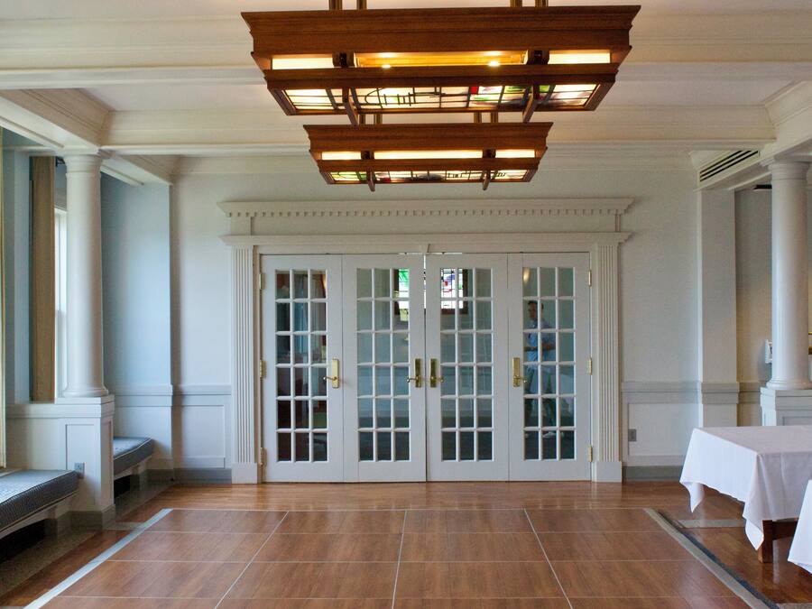 Een ruime lobby met een hoog plafond, een grote kroonluchter en een paar dubbele deuren met ruiten.