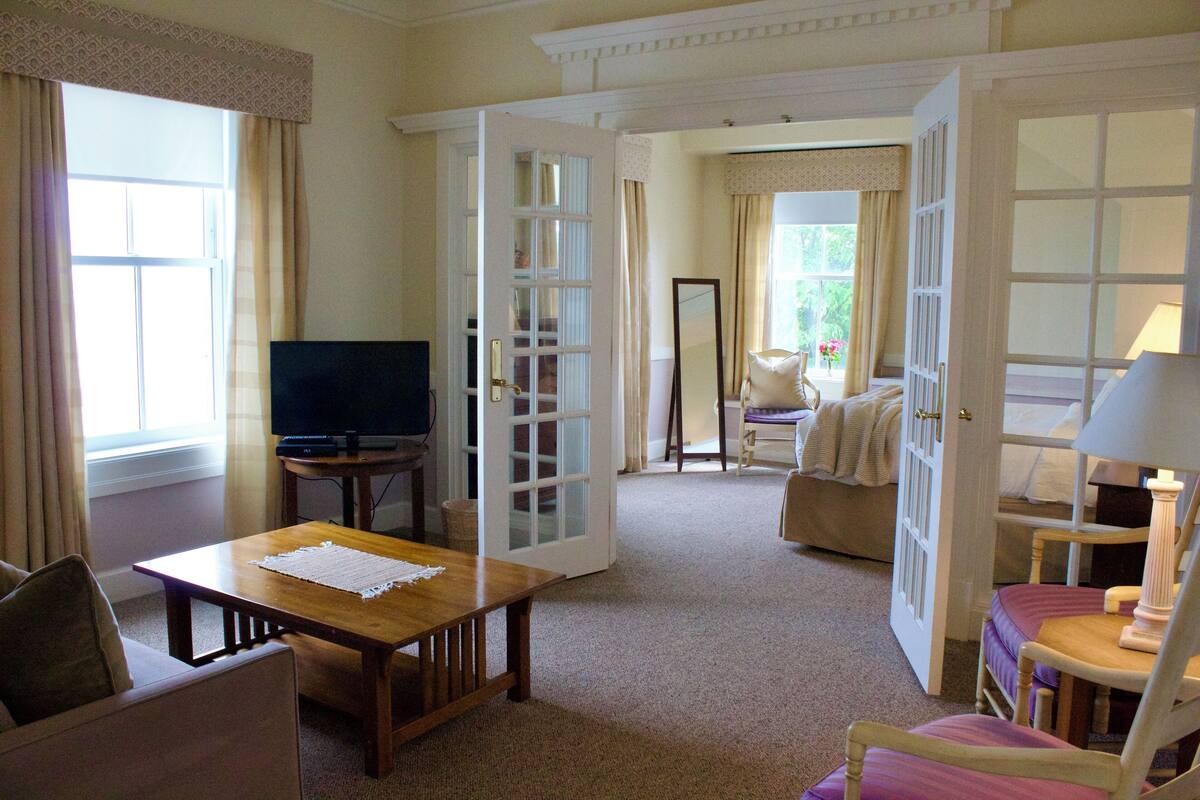 A hotel room with a wooden table, a sofa, a chair, a television, and a bed.