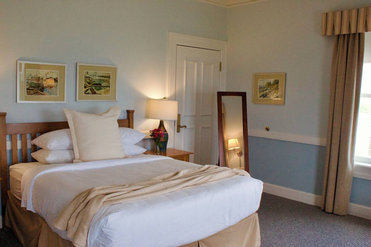 A neatly made bed with white linens, a nightstand with a lamp, and framed artwork on the walls.