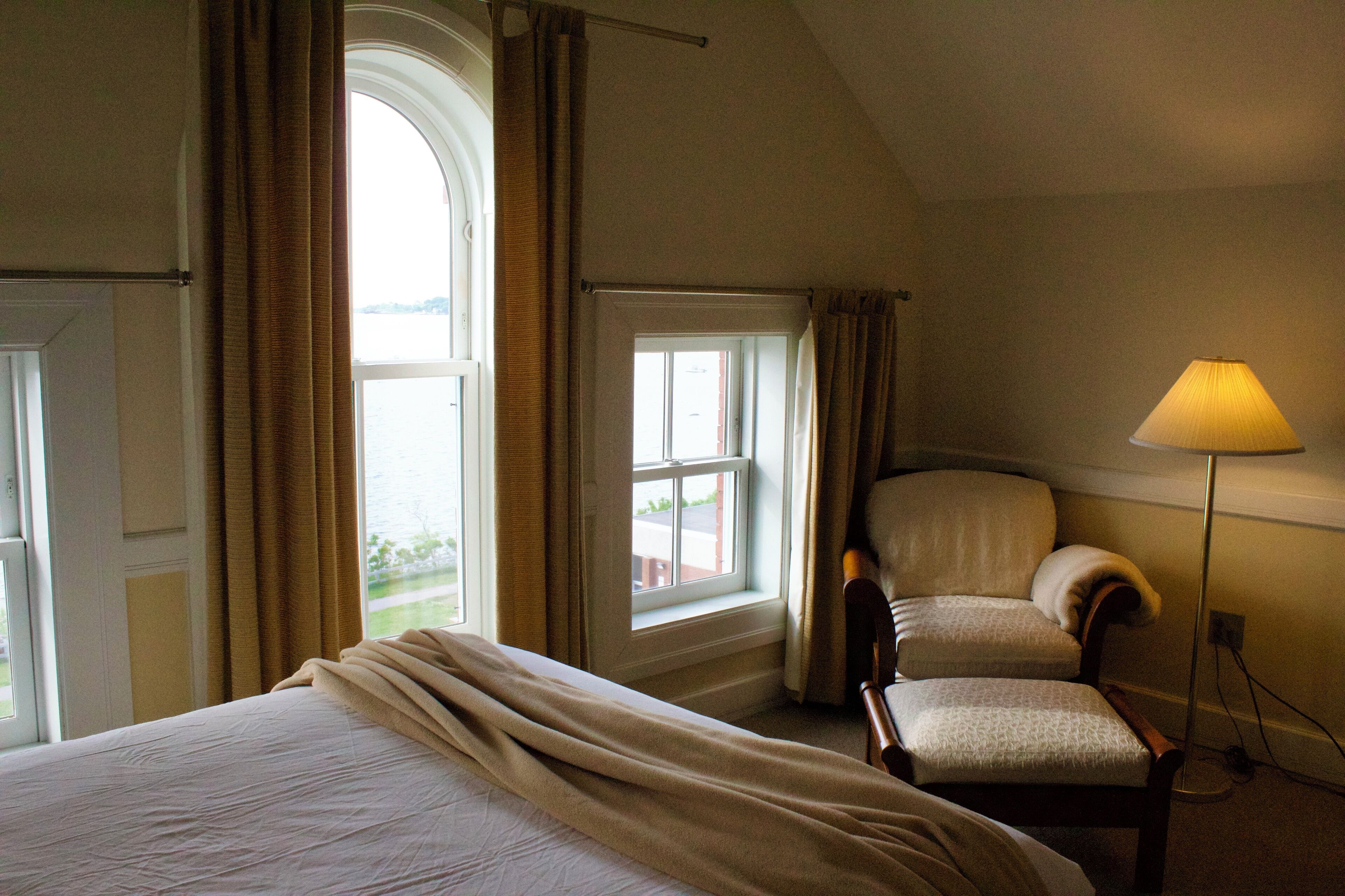 A hotel room with a bed, a chair, a lamp, and a window with curtains.
