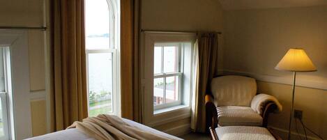A hotel room with a bed, a chair, a lamp, and a window with curtains.